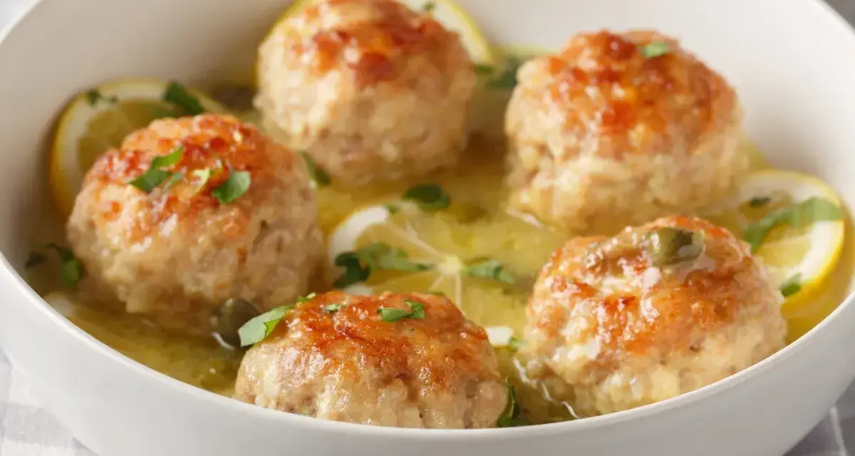 Polpette al limone dorate e succulente, servite in una ciotola bianca con fette di limone e prezzemolo tritato.
