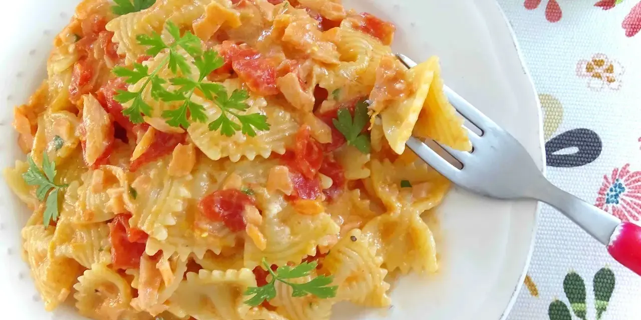 Farfalle cremose con pomodorini e salmone, guarnite con prezzemolo fresco. Un piatto invitante pronto per essere gustato.