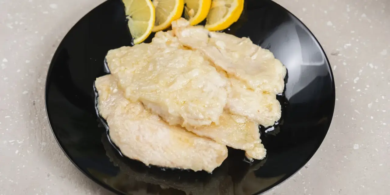Scaloppine di pollo al limone, un piatto classico e saporito, servite su un piatto nero con spicchi di limone fresco.