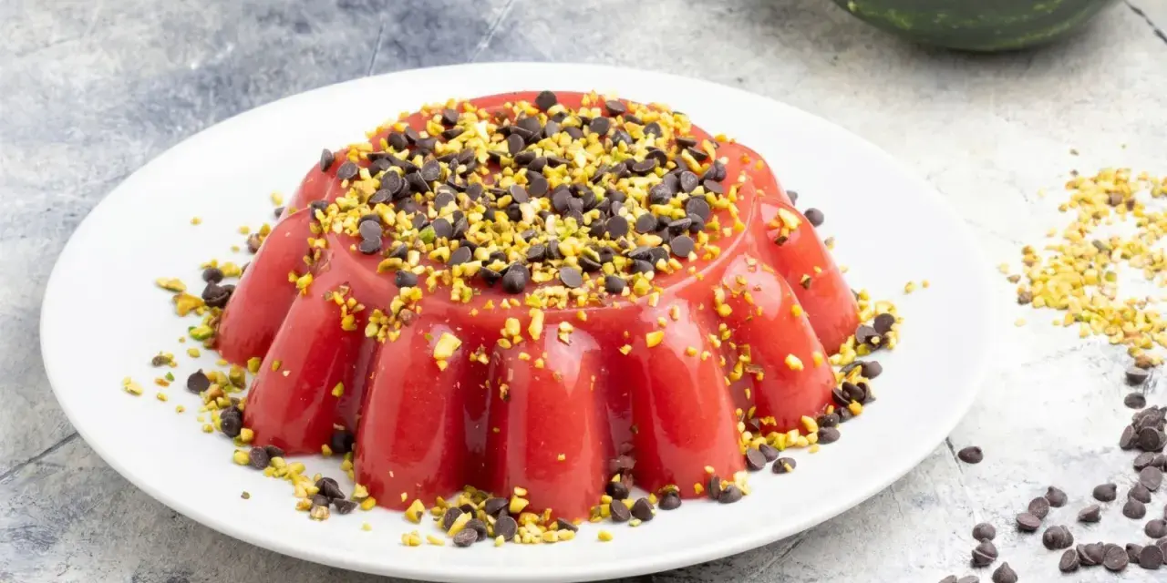 Delizioso gelo di melone rosso, guarnito con gocce di cioccolato e pistacchi tritati, su un piatto bianco.