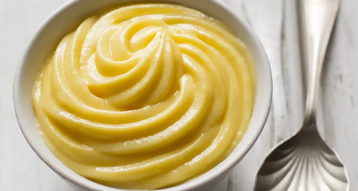 Una ciotola di soffice crema pasticcera, pronta per essere gustata. Accanto, un cucchiaio d'argento.