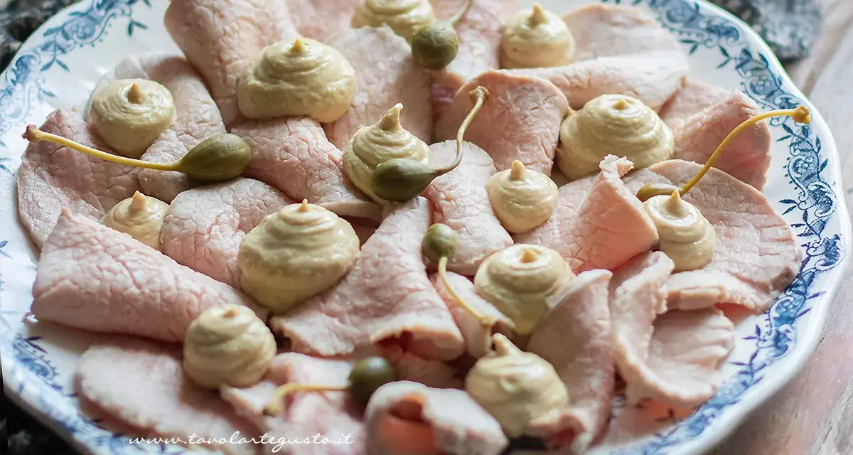 Piatto di vitello tonnato con salsa cremosa, capperi e guarnizioni.