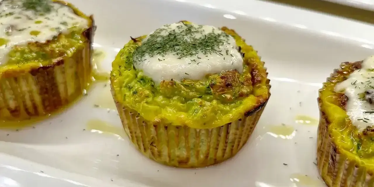Tre tortini di zucchine dorati, guarniti con formaggio fuso e aneto, serviti su un piatto bianco.