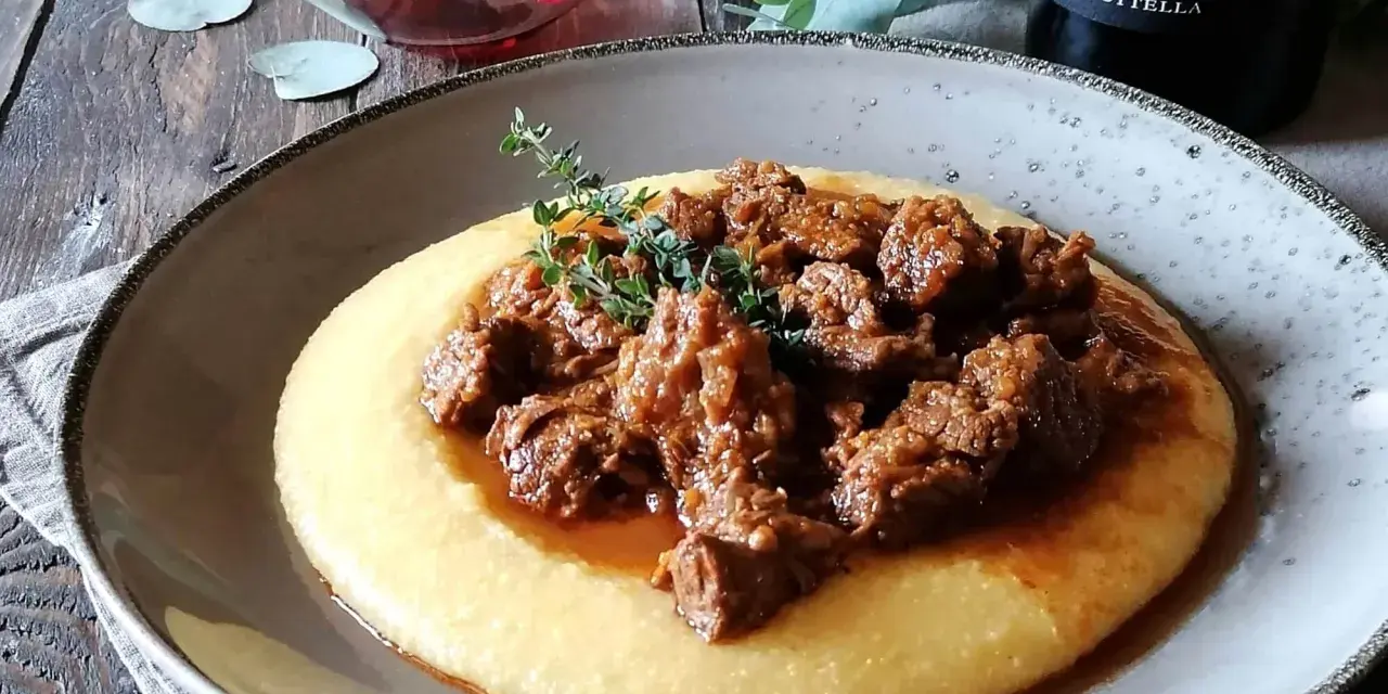 Un piatto di gulash con polenta fumante, guarnito con rametti di timo fresco. Un classico confortante, perfetto per una cena speciale.