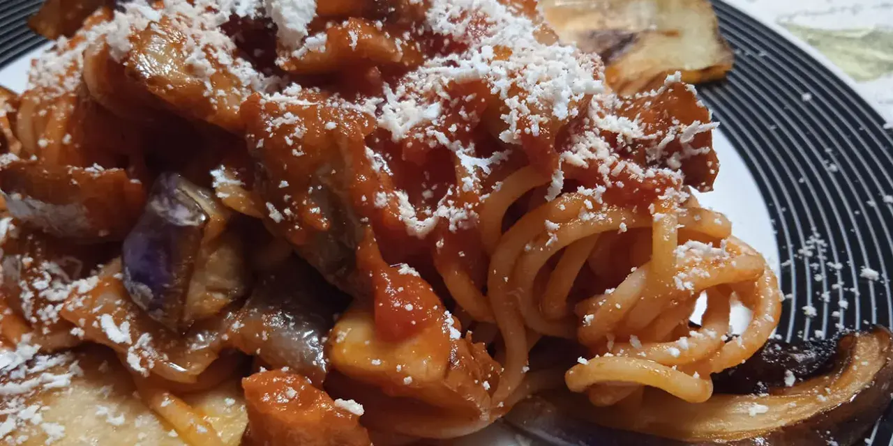 Un piatto invitante di pasta alla norma con melanzane fritte, sugo di pomodoro e ricotta salata grattugiata.
