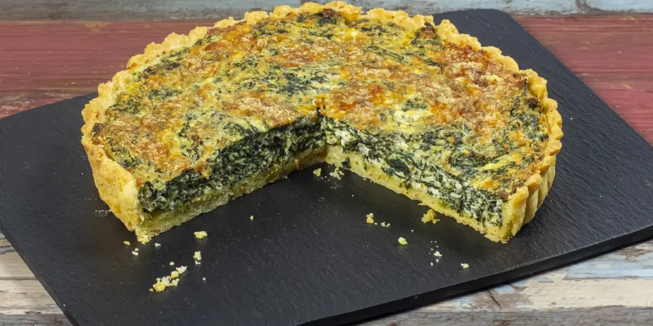 Una fetta di torta salata ricotta e spinaci, con crosta dorata e ripieno cremoso, su una lavagna scura.