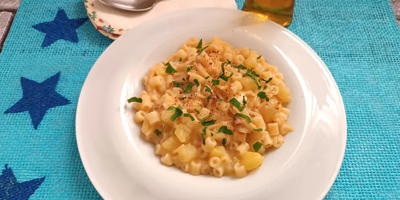 Un piatto di pasta patate e provola fumante, guarnito con prezzemolo fresco e un pizzico di peperoncino, pronto per essere gustato.