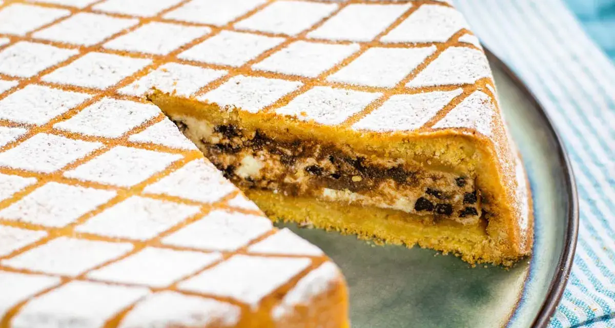 Una fetta di cassata al forno, con la sua copertura a rombi di zucchero a velo, rivela un ripieno goloso di ricotta e cioccolato.