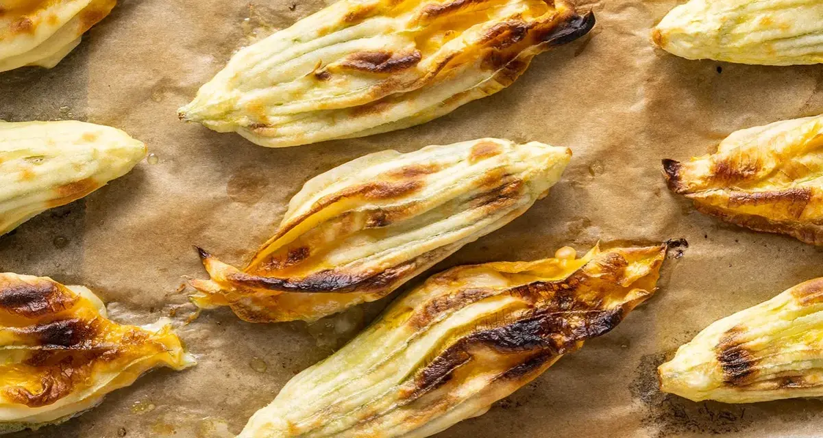 Fiori di zucca in pastella dorati e croccanti, appena sfornati su carta da forno.