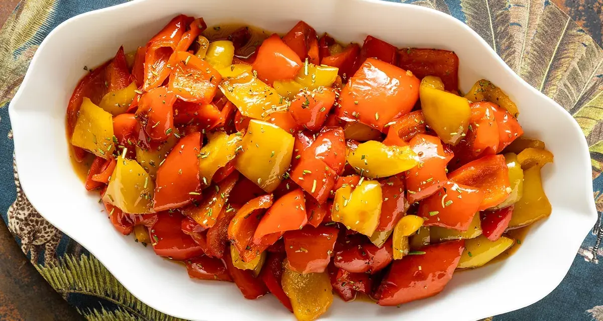 Peperoni in umido, colorati e succulenti, conditi con erbe aromatiche, serviti in una ciotola bianca su un tovagliolo decorato.