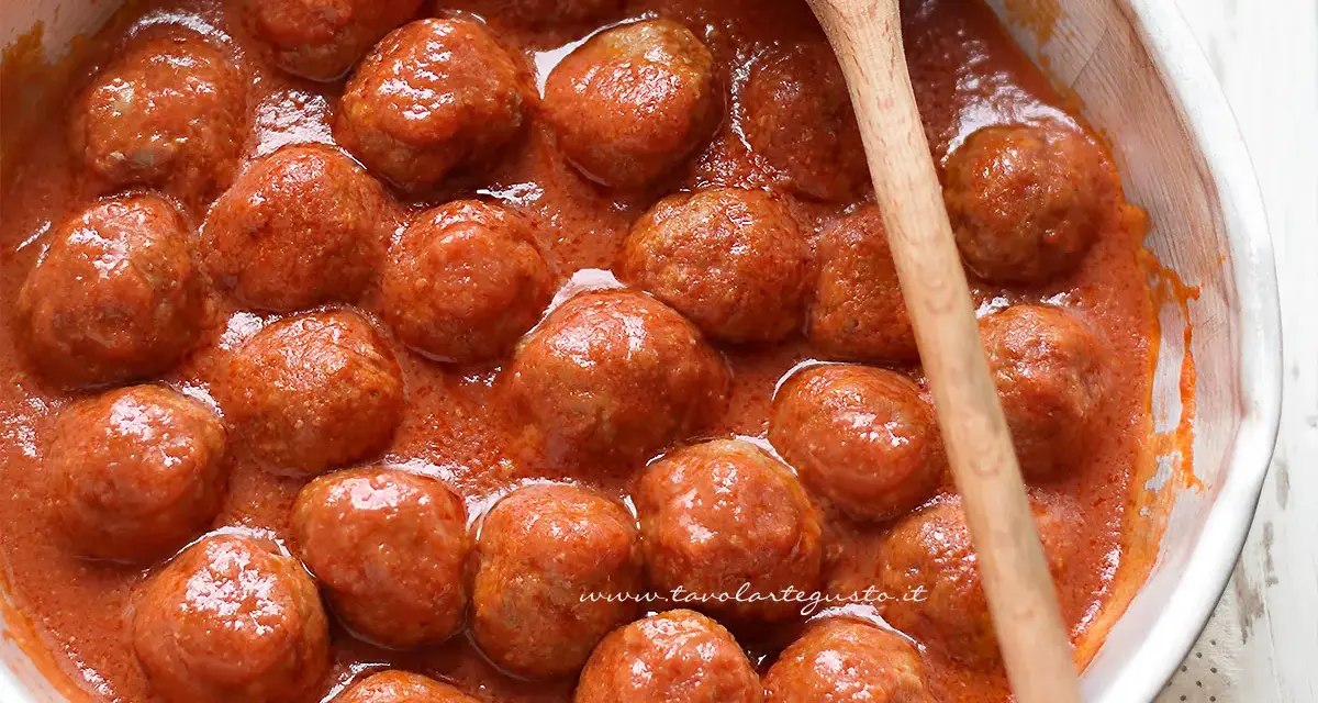 Succulente polpette di carne in un sugo rosso, pronte per essere gustate. Un cucchiaio di legno attende di servirle.