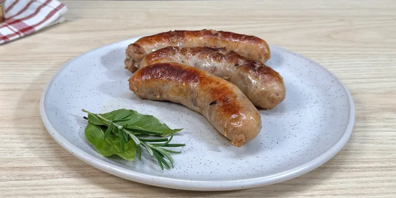 Tre salsicce dorate in padella, servite su un piatto con rosmarino e alloro.