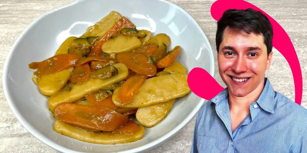 Un uomo sorride accanto a un piatto di gnocchi di riso con carote e zucchine.