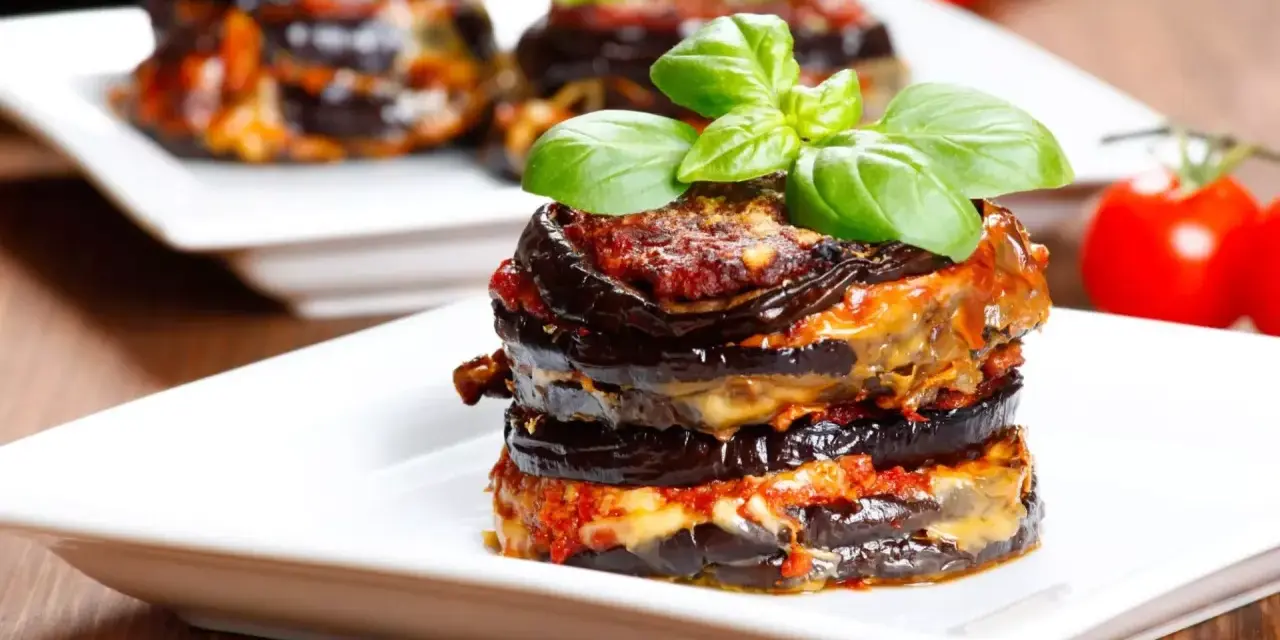 Parmigiana di melanzane, un classico della cucina italiana, servita su un piatto bianco con basilico fresco.
