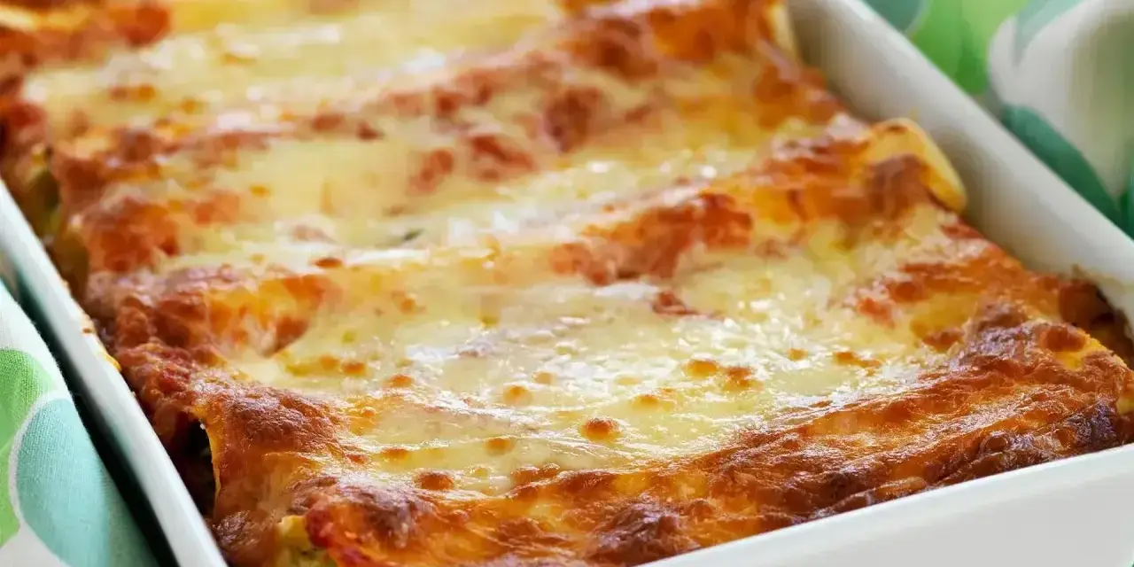 Cannelloni con ricotta appena sfornati, dorati e filanti, in una teglia bianca.