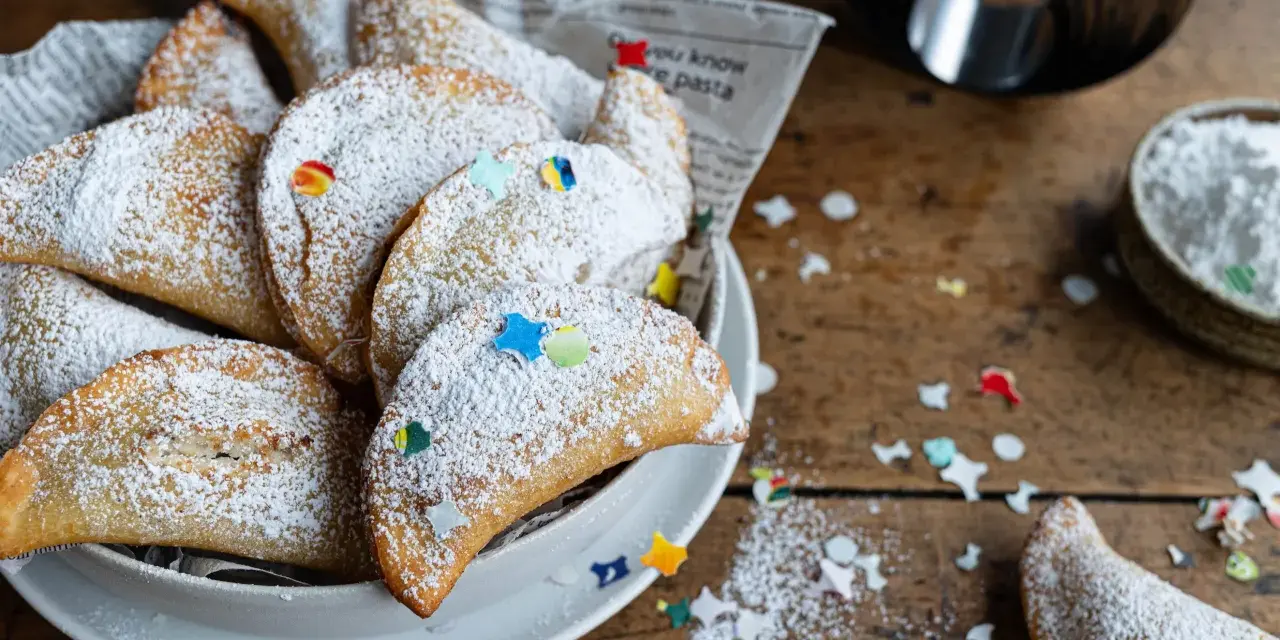 Cassatelle siciliane al forno, dolcetti dorati cosparsi di zucchero a velo e decorati con coriandoli colorati, pronti per essere gustati.