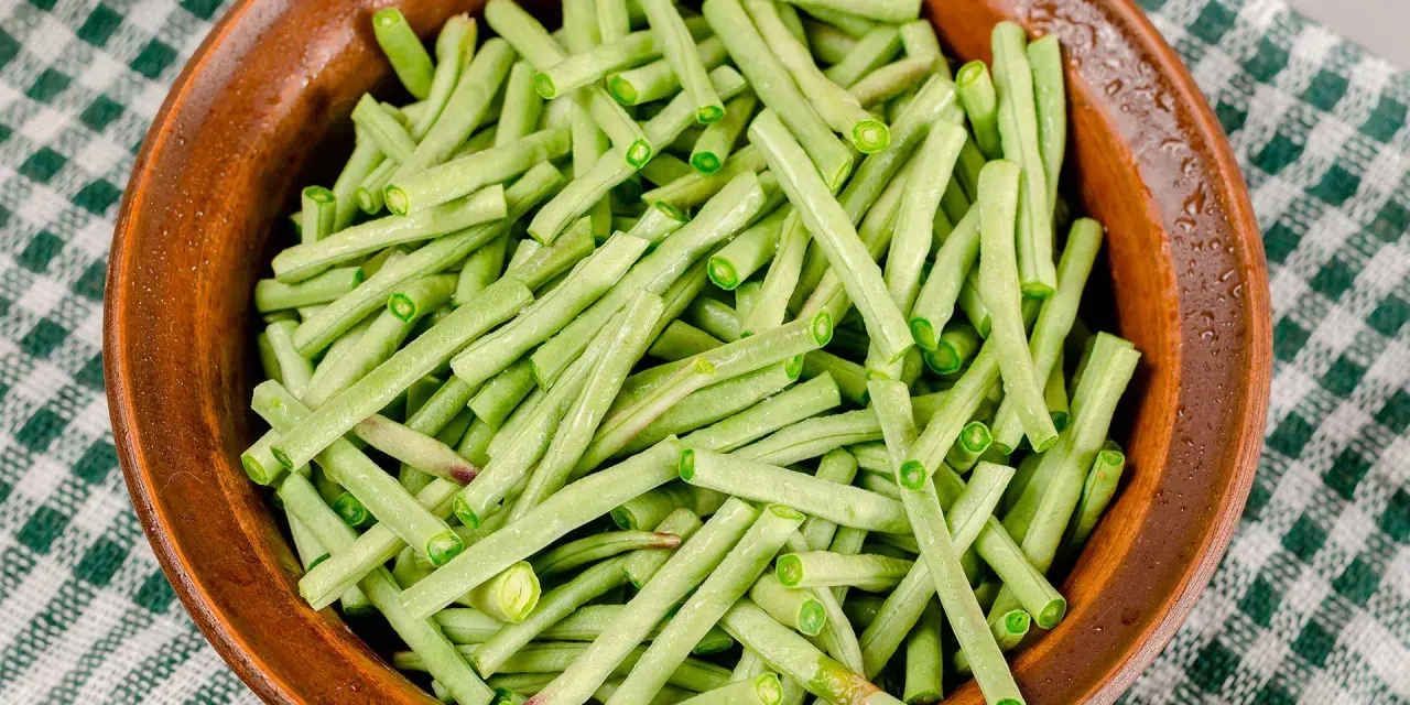 Fagiolini freschi, tagliati e pronti per essere cucinati in umido, in una ciotola di terracotta su una tovaglia a quadri verdi.