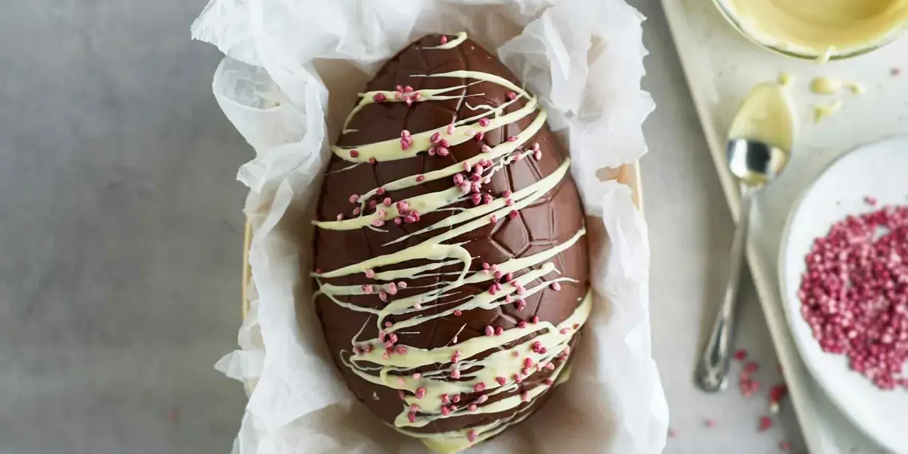 Un magnifico uovo di Pasqua fatto in casa, decorato con cioccolato bianco e granella rosa.