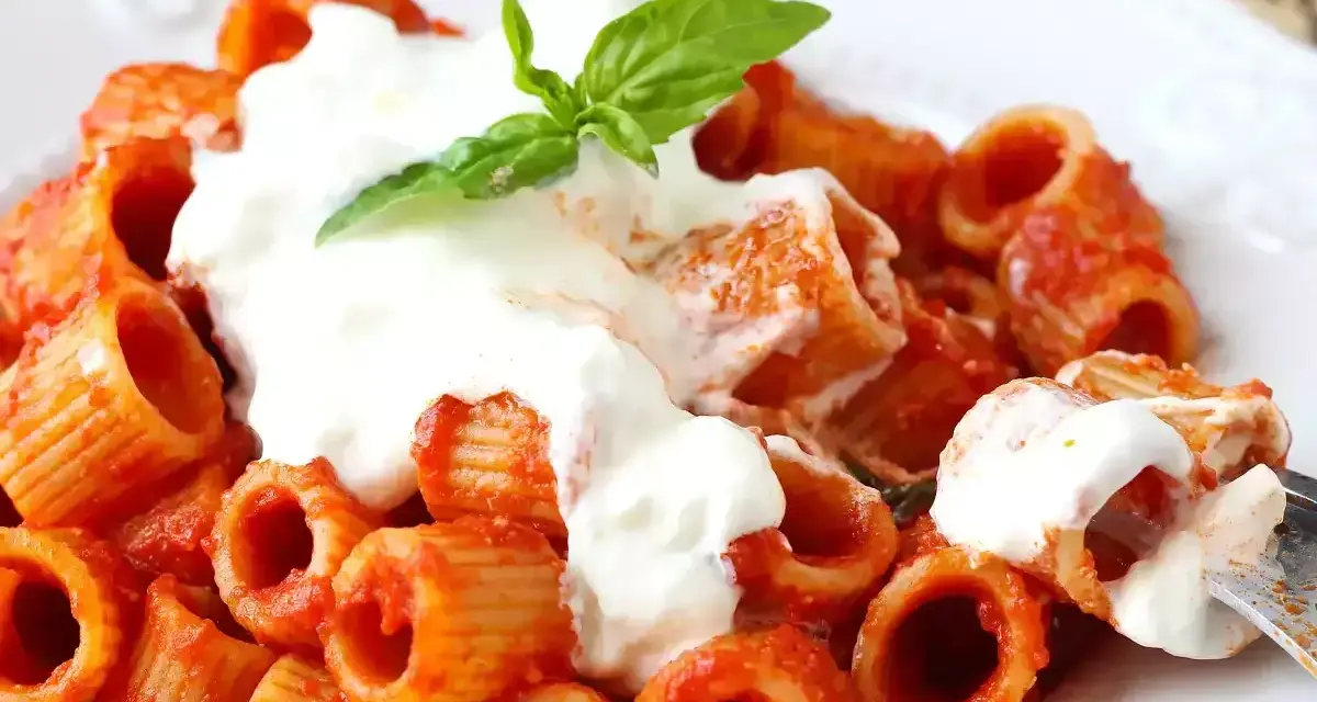 Rigatoni al sugo con abbondante stracciatella cremosa e una fogliolina di basilico fresco.