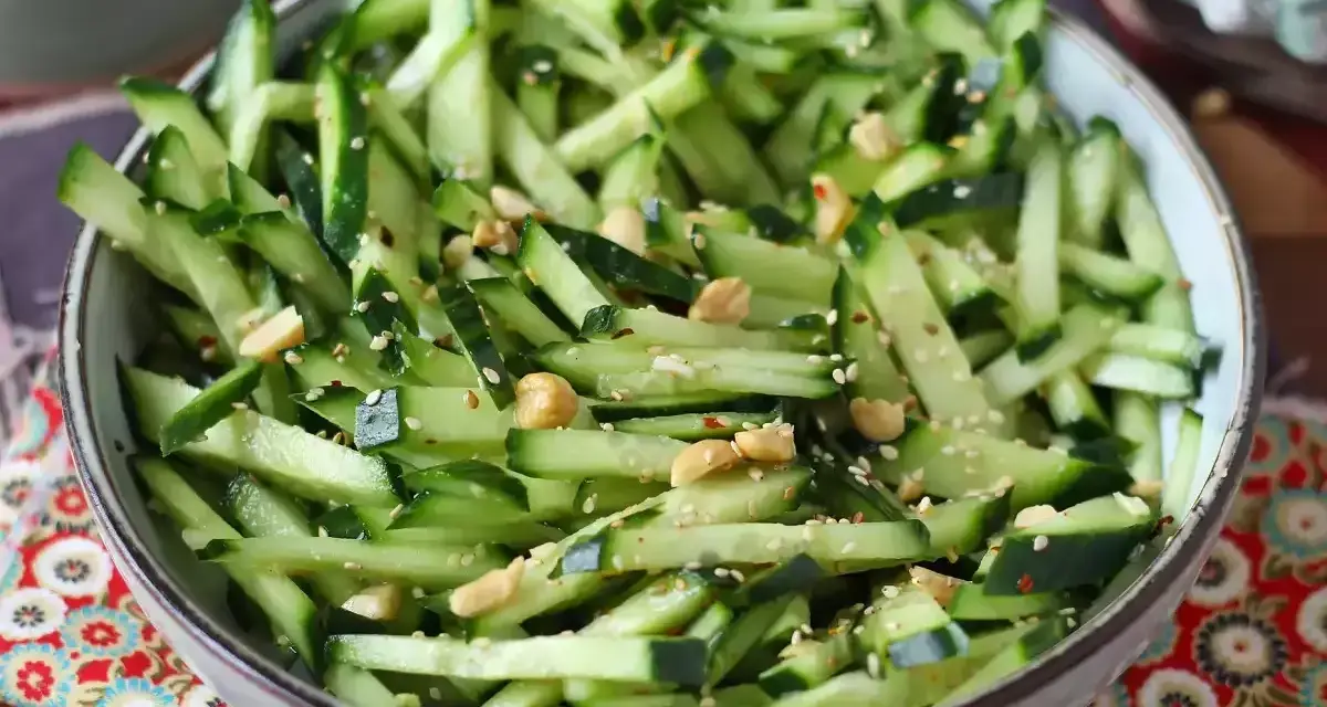 Una ciotola piena di fresca insalata di cetrioli tagliati a julienne, condita con semi di sesamo e arachidi croccanti.