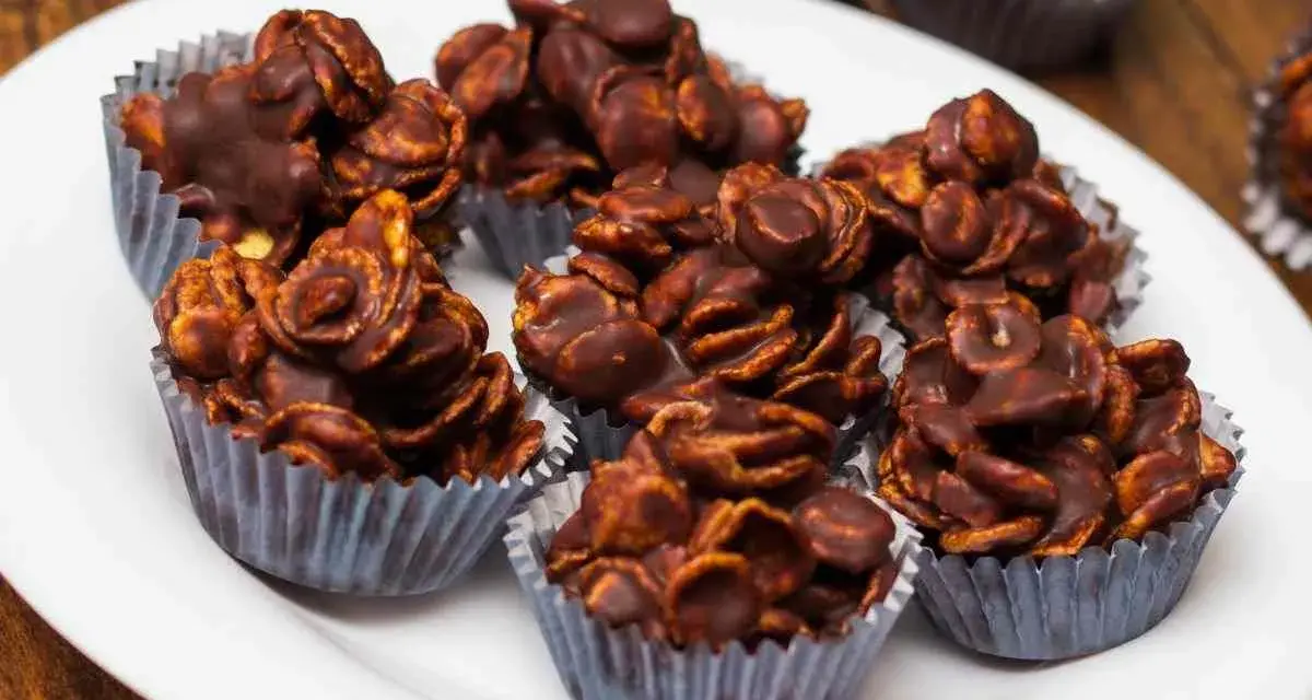 Deliziosi biscotti corn flakes e cioccolato, croccanti e golosi, serviti in pirottini argentati su un piatto bianco.