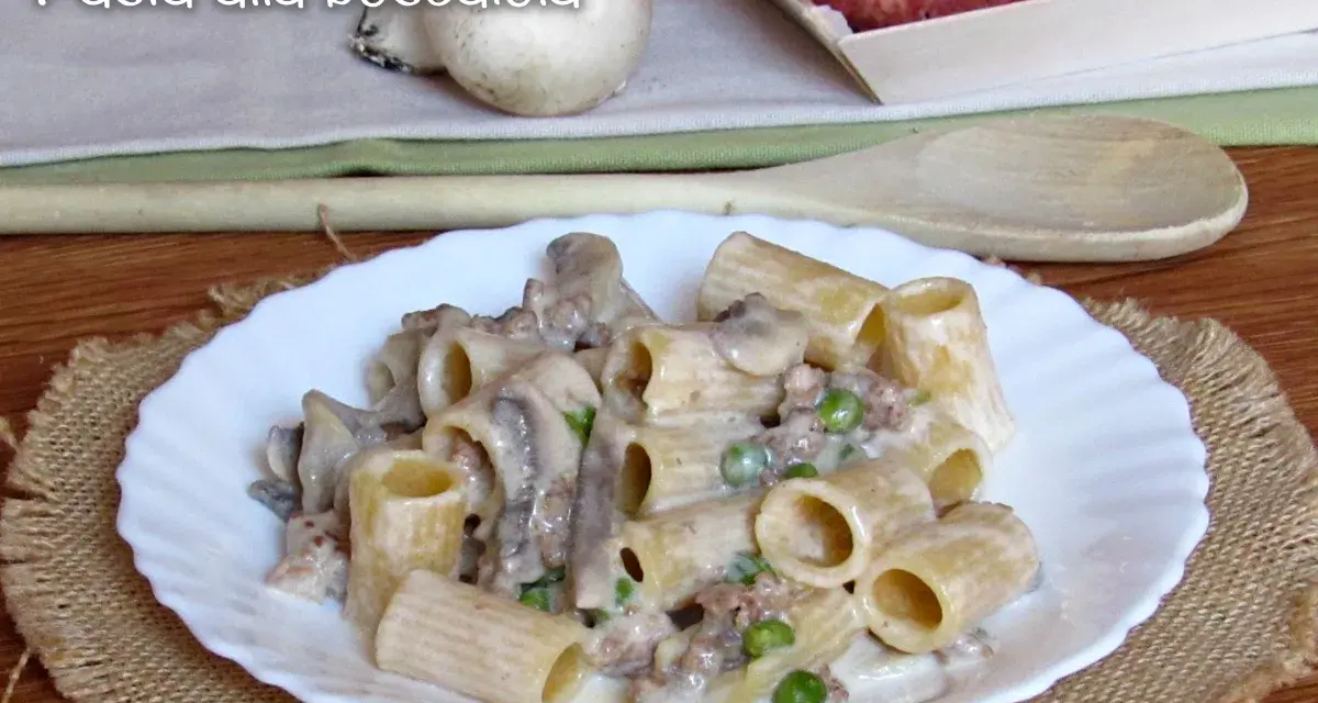 Piatto di pasta alla boscaiola con funghi, piselli e salsiccia, servita su un piatto bianco bordato.