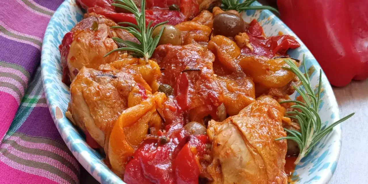 Un invitante pollo con peperoni alla siciliana, arricchito da olive e rosmarino, servito in un piatto decorato.