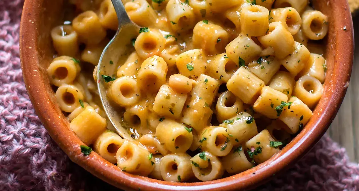 Un piatto invitante di pasta e fagioli estiva, condita con erbe fresche, servita in una ciotola di terracotta.