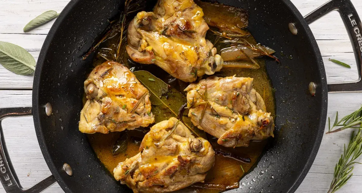 Cosce di pollo in padella, dorate e succulente, con erbe aromatiche e un sughetto invitante.