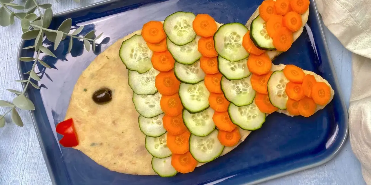 Un simpatico pesce finto ricetta, con corpo di purè, scaglie di cetriolo e carota, occhio d'oliva e bocca di peperone rosso.
