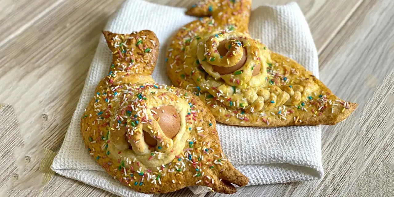 Due cuddure cu l'ova, dolci pasquali decorati con zuccherini colorati, riposano su un panno bianco.