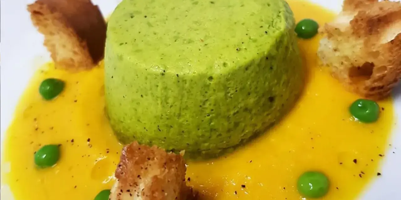 Sformato di piselli verde brillante su crema gialla, guarnito con piselli freschi e crostini dorati.