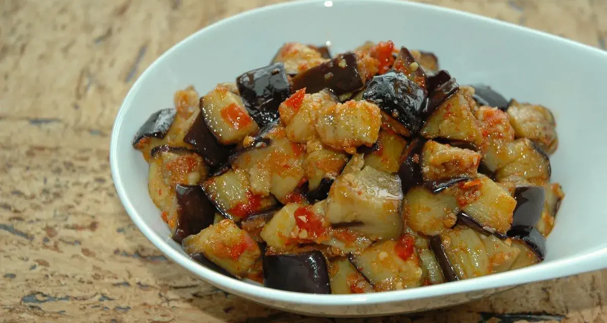 Melanzane al microonde, tagliate a cubetti e condite con pomodoro e spezie, servite in una ciotola bianca.