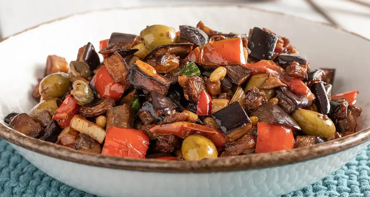 Caponata ricetta: melanzane, peperoni, olive e capperi in un piatto invitante.