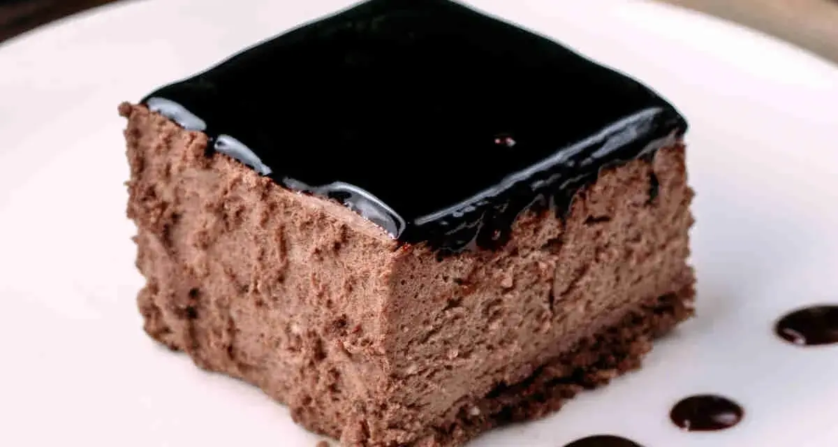 Un delizioso semifreddo al cioccolato, con una lucida glassa scura e gocce di salsa al cioccolato sul piatto bianco.