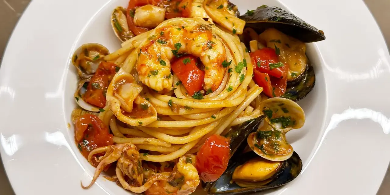 Un piatto invitante di spaghetti allo scoglio, con gamberi, cozze, vongole e calamari, condito con pomodorini freschi e prezzemolo.