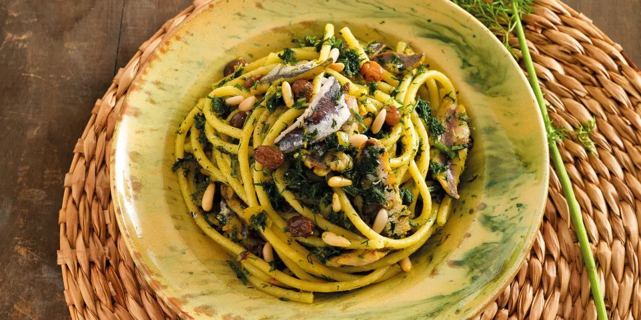 Un piatto di pasta con le sarde, condita con finocchietto selvatico, pinoli e uvetta, servita in un piatto decorato.