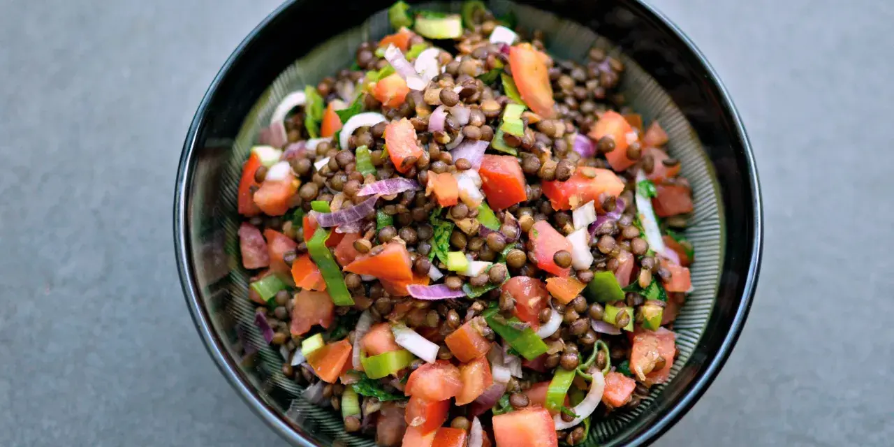 Una ciotola di insalata di lenticchie colorata con pomodori, cipolla rossa e erbe fresche.