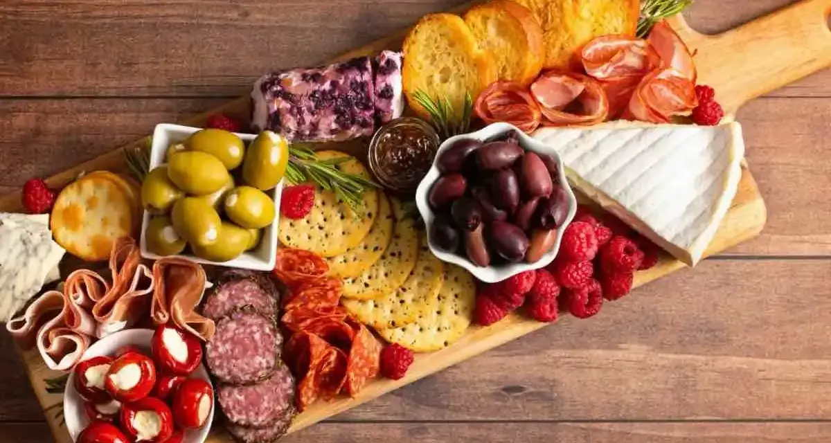 Un invitante tagliere salumi e formaggi con olive, lamponi, pane tostato e formaggio cremoso, perfetto per un aperitivo.