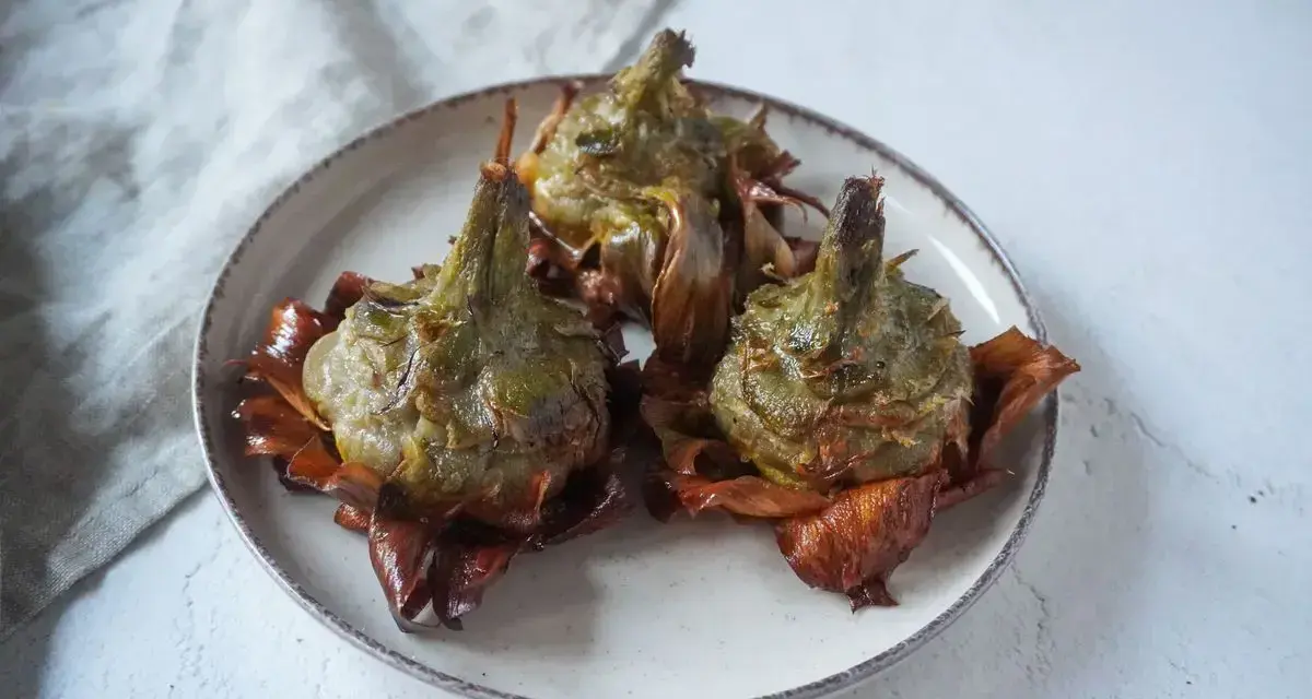 Tre carciofi alla giudia dorati e croccanti su un piatto, pronti per essere gustati.