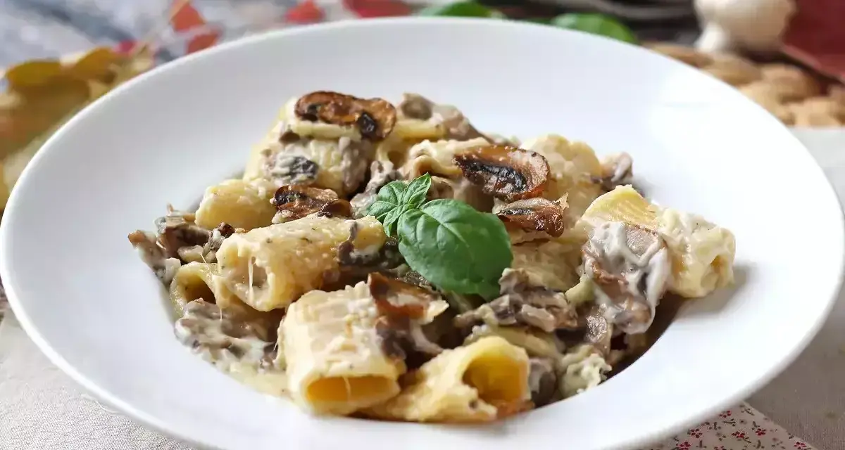 Un piatto invitante di pasta funghi e panna, con rigatoni conditi generosamente e guarniti con basilico fresco.