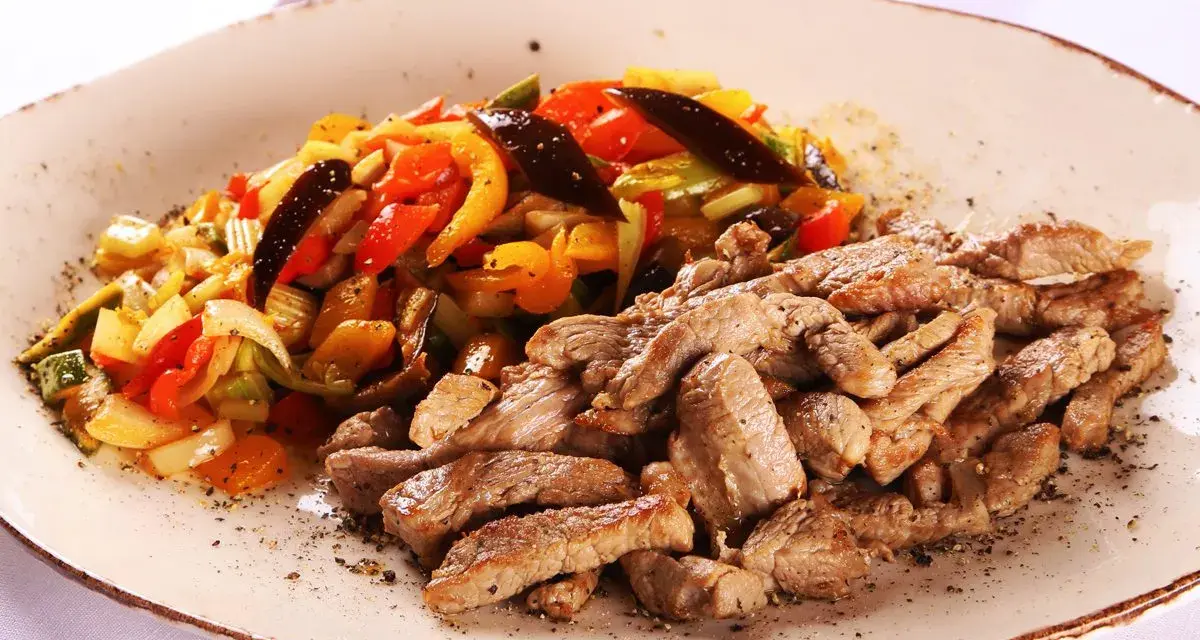Straccetti di vitello succulenti serviti con un contorno colorato di verdure saltate, un piatto invitante e saporito.