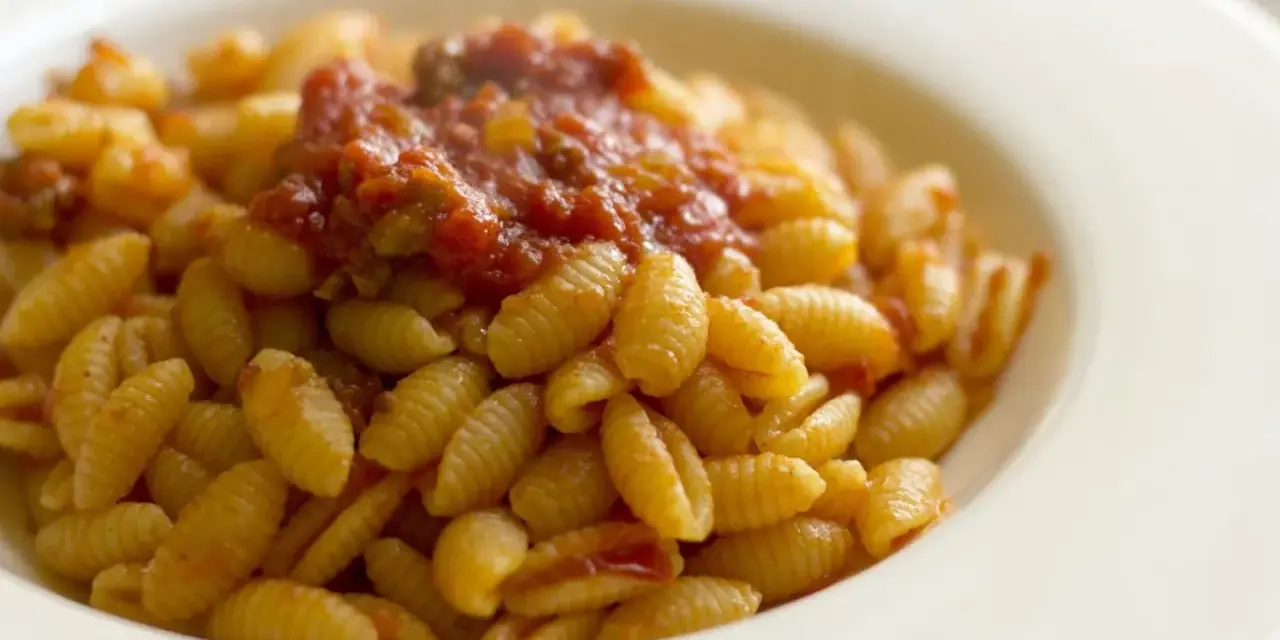 Malloreddus alla campidanese, pasta sarda con sugo di pomodoro e salsiccia, serviti in un piatto bianco.