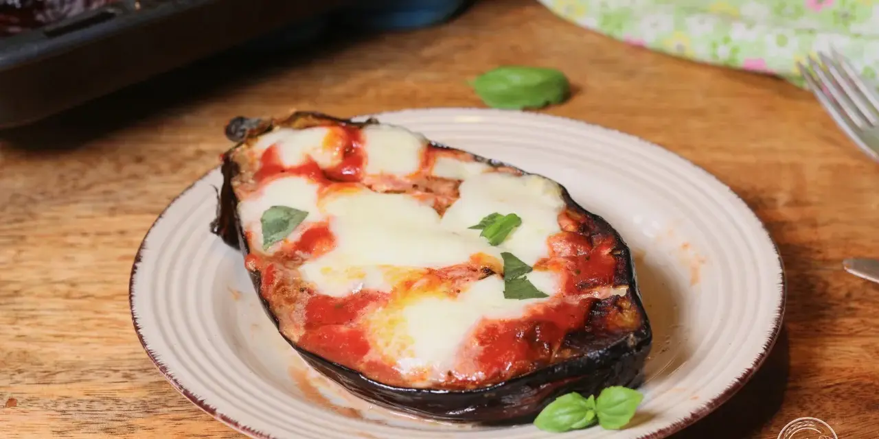 Melanzane alla pizzaiola appena sfornate, con mozzarella filante e basilico fresco su un piatto rustico.