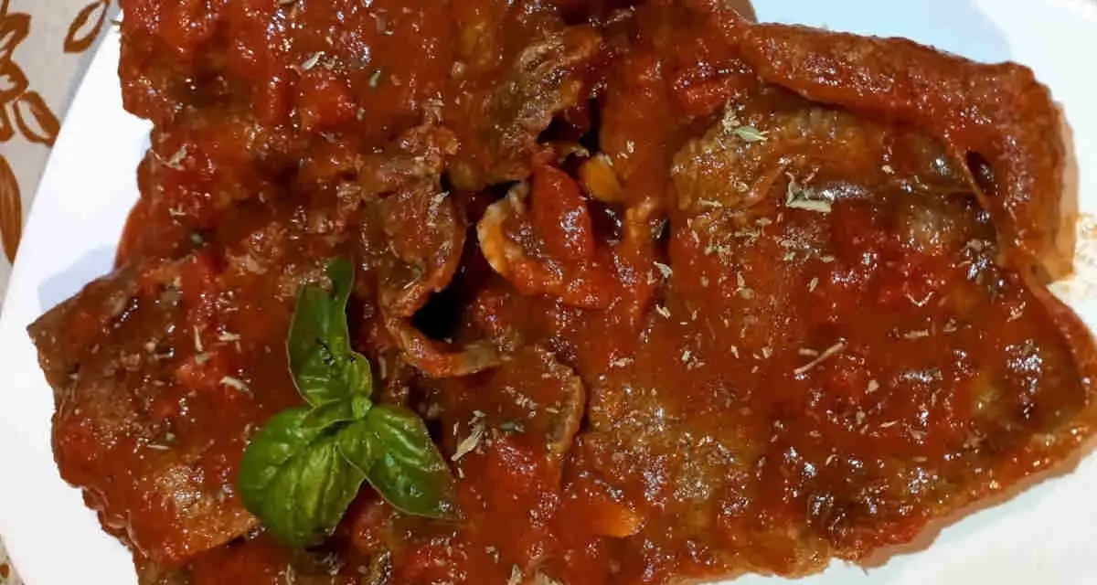 Fette di carne alla pizzaiola, ricoperte da un sugo rosso saporito e guarnite con basilico fresco.