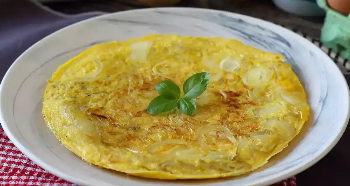 Una dorata frittata di cipolle, guarnita con basilico fresco, servita su un piatto bianco.