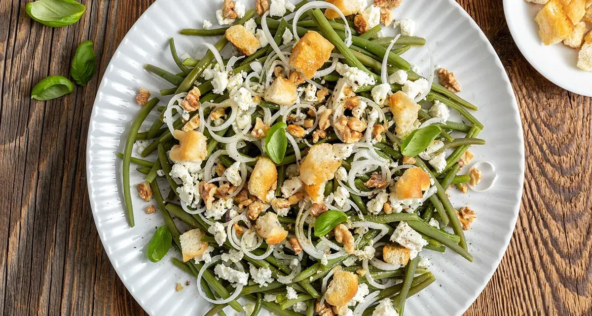 Deliziosa insalata di fagiolini con formaggio feta, noci croccanti, crostini e cipolla rossa. Un piatto fresco e saporito.