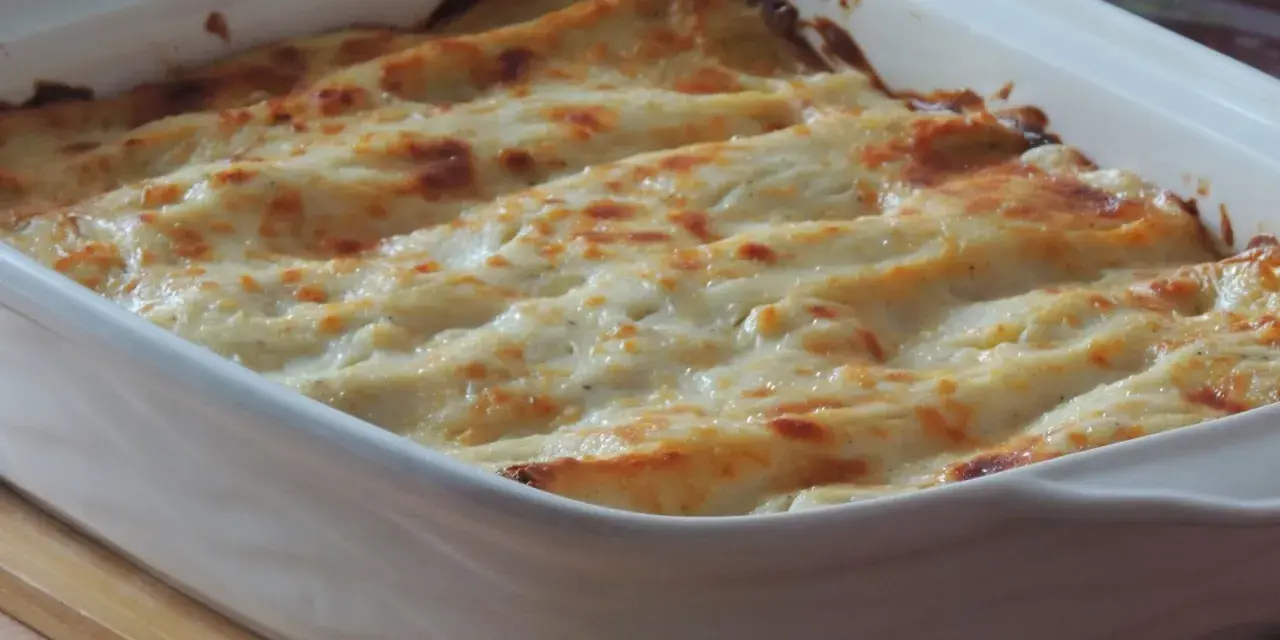 Lasagne con carciofi, besciamella e mozzarella appena sfornate, dorate e filanti in una teglia bianca.