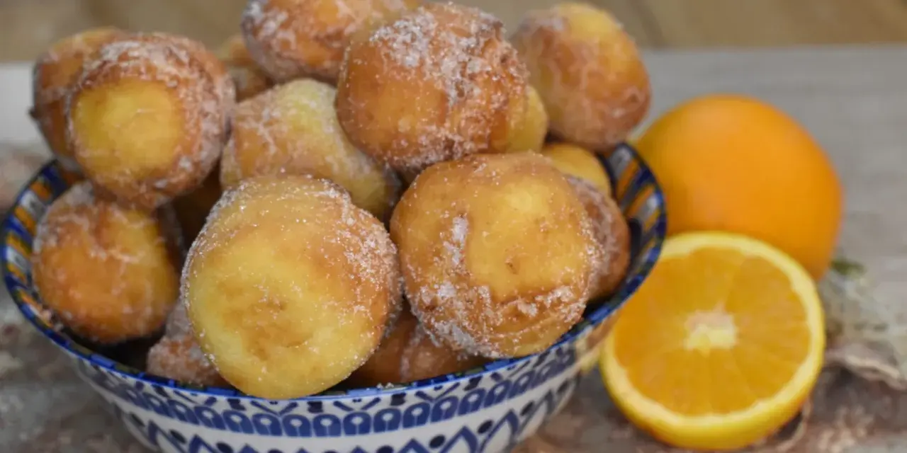 Arancini dolci, soffici arrubiolus di ricotta cosparsi di zucchero, accanto a fette d'arancia.