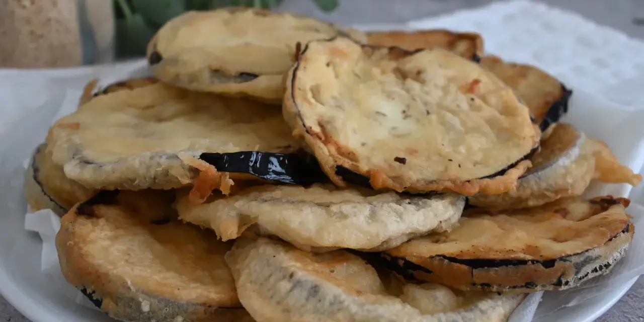 Piatto di melanzane fritte pastellate, dorate e croccanti, pronte per essere gustate.